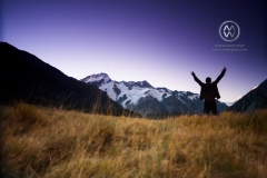 New Zealand's Aoraki / Mount Cook village is located in the central part of the South Island, deep in the heart of the Southern Alps. A man raises his arms in joy as he watches the stunning sunset in the center of the park.