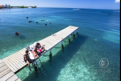 Girls play music and enjoy the sun on a Utila dock in front of Trudy's Hotel.