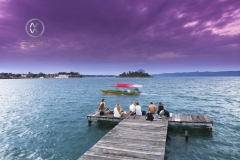 A beautiful sunset along the Lake Peten River in Flores. Friends sit at the end of the pier to watch.