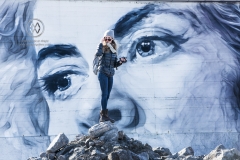 A girls stands in front of an outdoor mural on one of Reykjavik's buildings. The artist is Guido Van Helten.