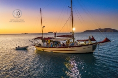Sailing through the Whitsunday Islands is one of the most popular attractions in Australia. A sailboat anchors in a calm harbor at sunset.