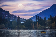 Sunset descends over Queenstown's Lake Wakatipu. A man kayak's under a full moon.
