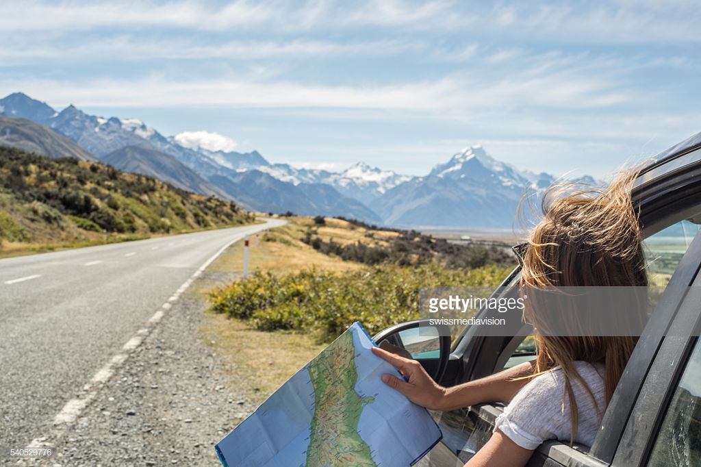 Portrait of a young woman in a car looking at a map for directions.