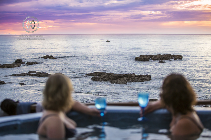 Girls sit and enjoy a glass of wine from a spa pool at sunset on the New Zealand coastline in the city of Te Kaha.