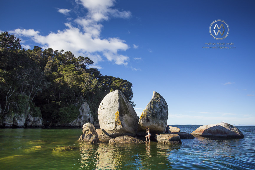 A woman poses in front of one of New Zealand's famous landmarks; Able Tasman National Park's Split Apple Rock.