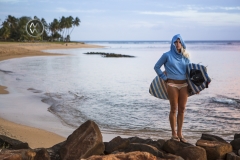 A surfer girls walks out to sea to check out the surf at sunset.