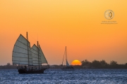 A sailboat crosses the Utila harbor at sunset.