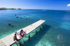 Girls play music and enjoy the sun on a Utila dock in front of Trudy's Hotel.
