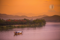 A fishing boat floats down the Perfume River at sunset.