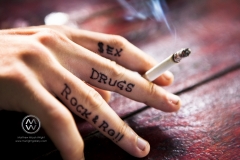 A man has an interesting tattoo on the insides of his fingers and it says " sex, drugs, rock & roll".