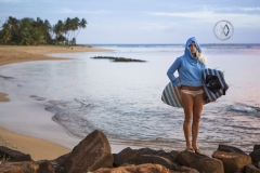 A surfer girls walks out to sea to check out the surf at sunset.