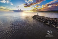 A surfer girls walks out to sea to check out the surf at sunset.