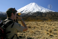 The Tongariro Crossing is considered by many to be the finest "one day walk" in New Zealand, if not the world.  The trail takes hikers through a volcanic plateau of old lava flows, volcanic craters, and gives allows the opportunity to walk between a field of three active volcanoes; Mt Tongariro, Ruapehu, and Ngauruhoe (which stars as the Lord of the Ring's Mount Doom). The ground steams with geothermal heat, and steam often rises from the active volcanoes cones. Here a group of hikers embrace and take in the spectacular views of the plateau and Mt. Ngauruhoe.