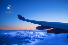 A plane flies above the clouds at sunset.